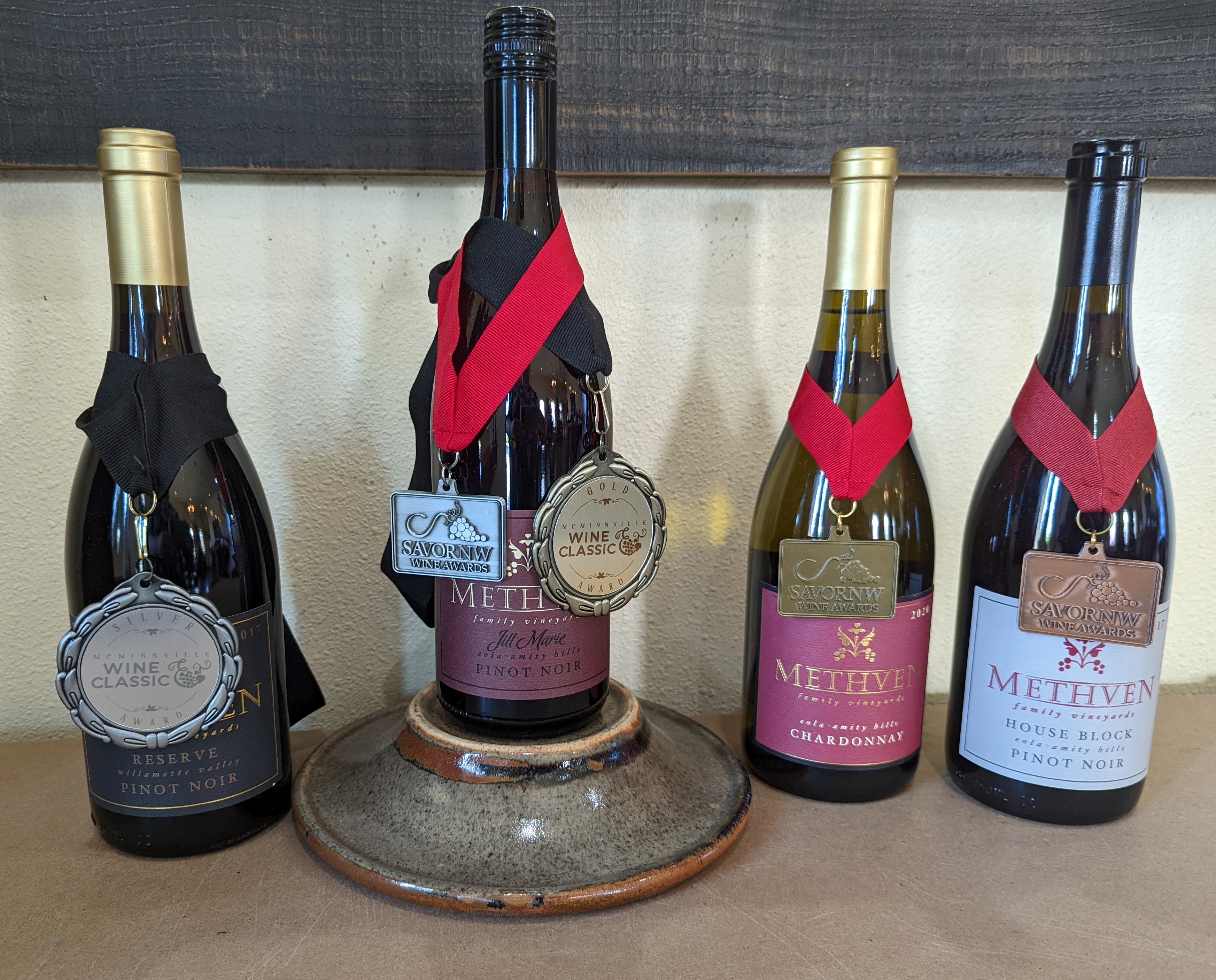 A display of our award-winning wine bottles with their respective medals on the bottle necks. From left to right: 2017 Reserve Pinot Noir, 2017 Jill Marie Pinot Noir, 2020 Chardonnay, and 2017 House Block Pinot Noir.